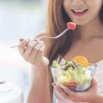 Healthy food healthy lifestyle with young happy woman eating green fresh ingredients organic salad. Vegan girl holding salad bowl with smiling face eating healthy diet food.