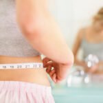 Closeup of a young woman measuring her waist in the bathroom